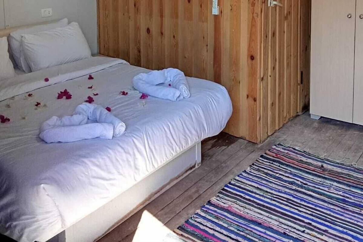 Een slaapkamer met een houten garderobe, een bed met witte lakens, een dromenvanger en een hanglamp.