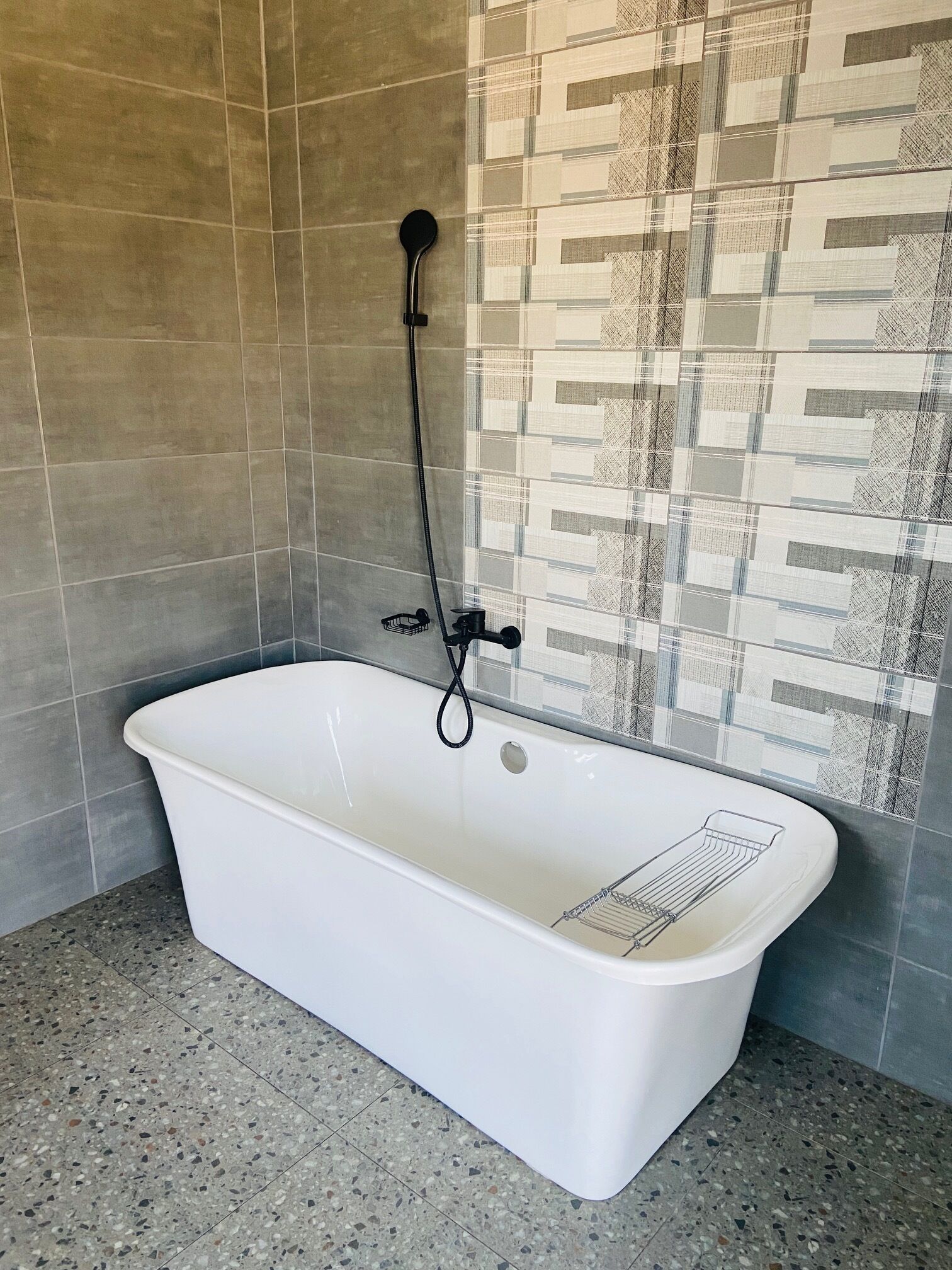 Un baño con una bañera blanca, un cabezal de ducha y una pared de azulejos con un diseño geométrico.