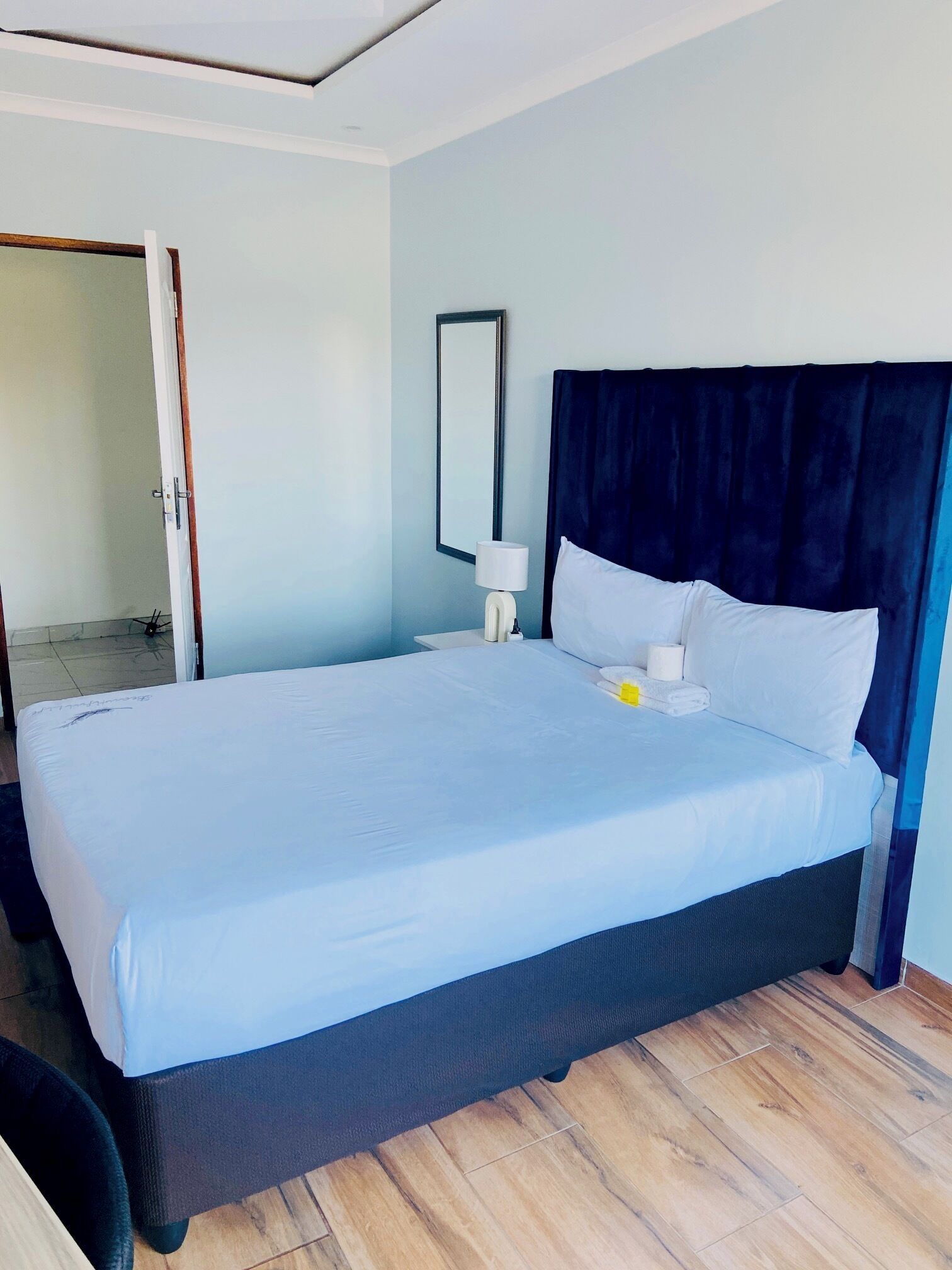 A hotel room with a large bed, a bedside table with a lamp, and a door leading to another room.