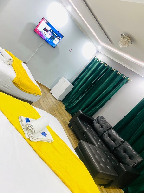 A hotel room with two beds, a black leather sofa, a flat-screen TV mounted on the wall, and green curtains. - Airport Imperial Guest House (Kempton Park)
