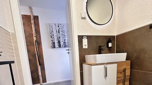 Ein Badezimmer mit einem weißen Waschbecken, einem Holfläschchen und einem runden Spiegel an der Wand.