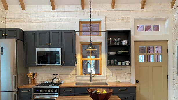 Eine moderne Küche mit dunklen Schränken, Edelstahlgeräten, einer Holzausziehtafel und einem Fenster über der Spüle.