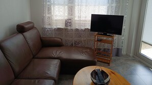 Una sala de estar con un sofá de cuero marrón, un televisor sobre un mueble de madera y una cortina estampada.