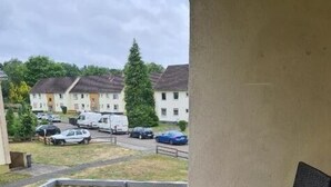 Un balcón con una mesa y sillas, vistas a coches aparcados y edificios al fondo.
