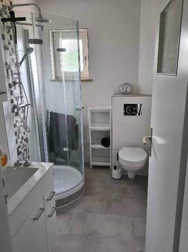 Un baño pequeño con ducha de mampara de vidrio, inodoro y lavabo.