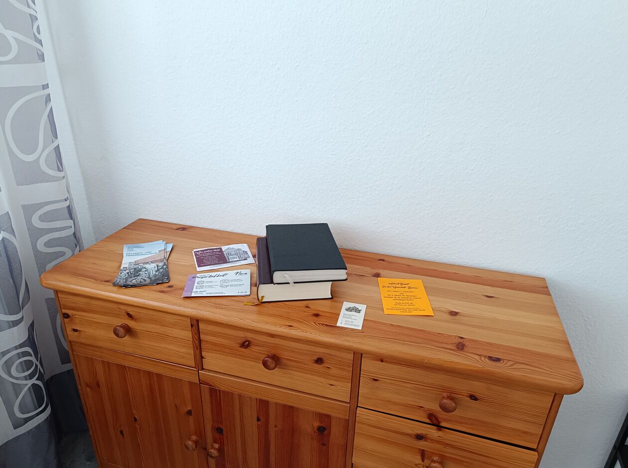 A wooden dresser with a black book, a pamphlet, and a yellow note on top.