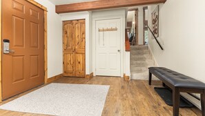 Un couloir doté d’un plancher en bois, d’une porte blanche, d’un banc et d’un escalier menant à une autre pièce.