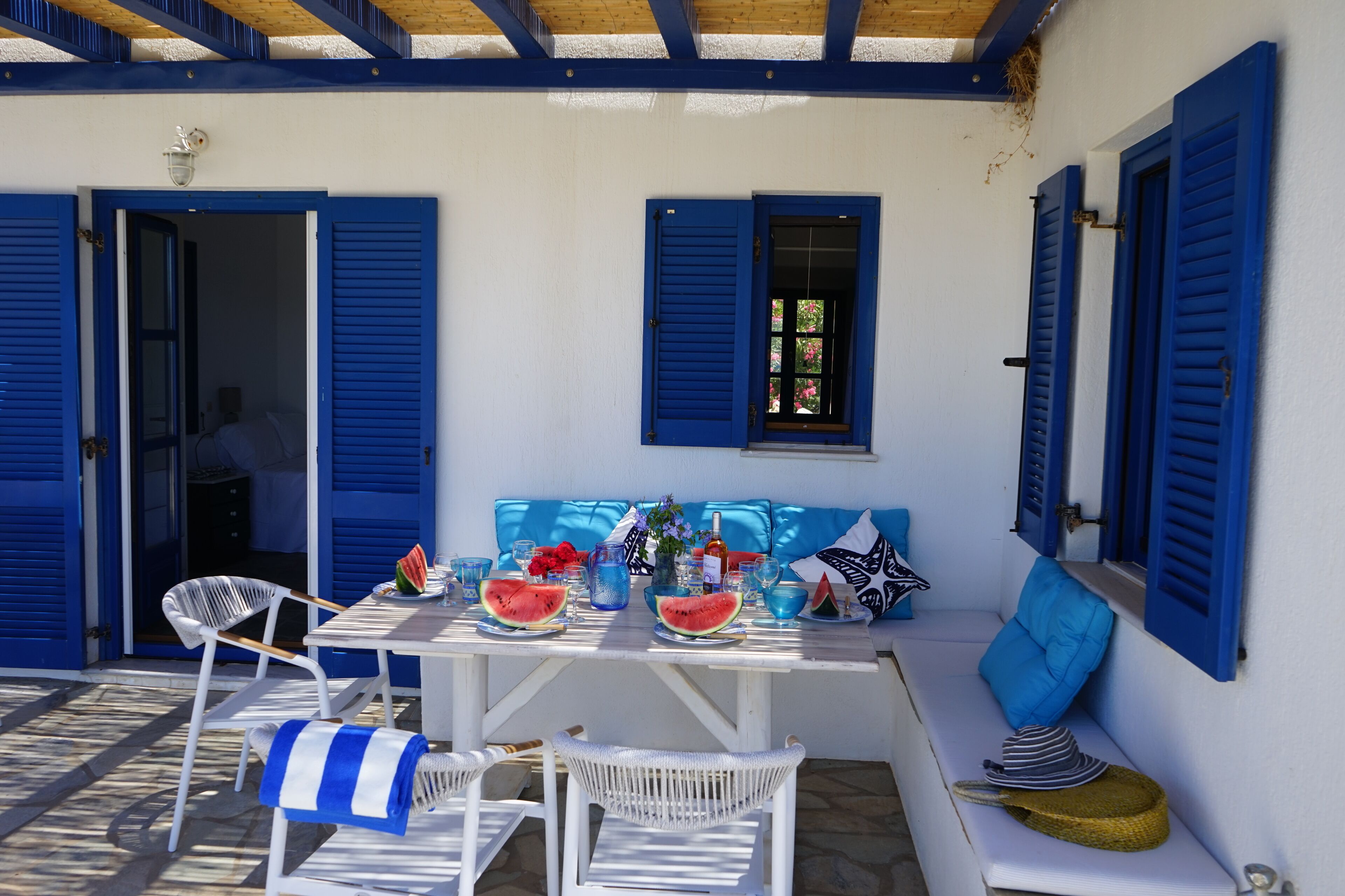 Un espace extérieur aménagé avec une table pour deux, décoré dans des tons de bleu et de blanc, comprenant une chaise en osier et un banc avec des coussins.