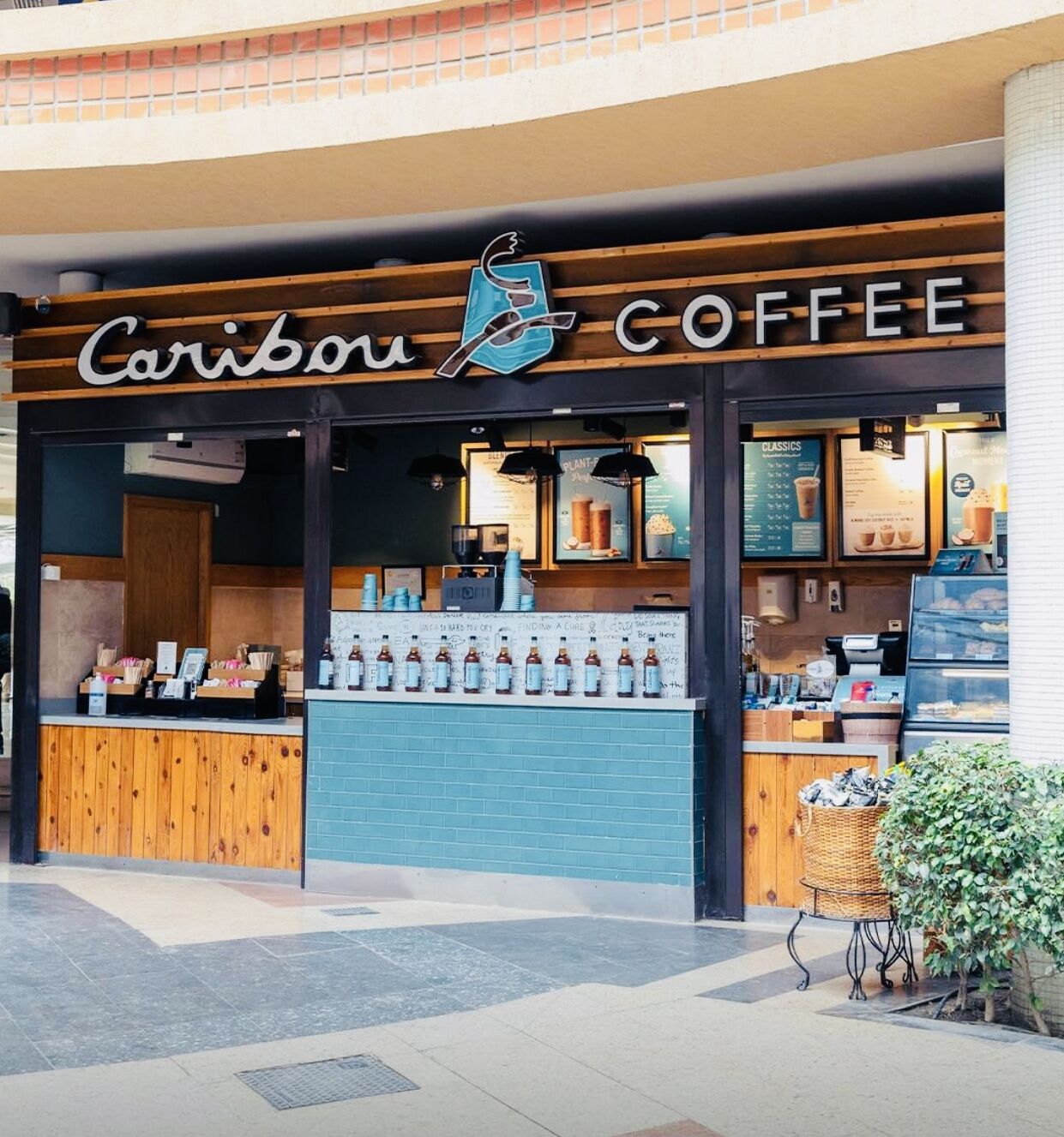 Caribou Coffee -niminen kahvila, jonka julkisivu on puuta, siinä on sinisillä laatoilla koristeltu seinä ja esillä on pulloihin pakattuja juomia.