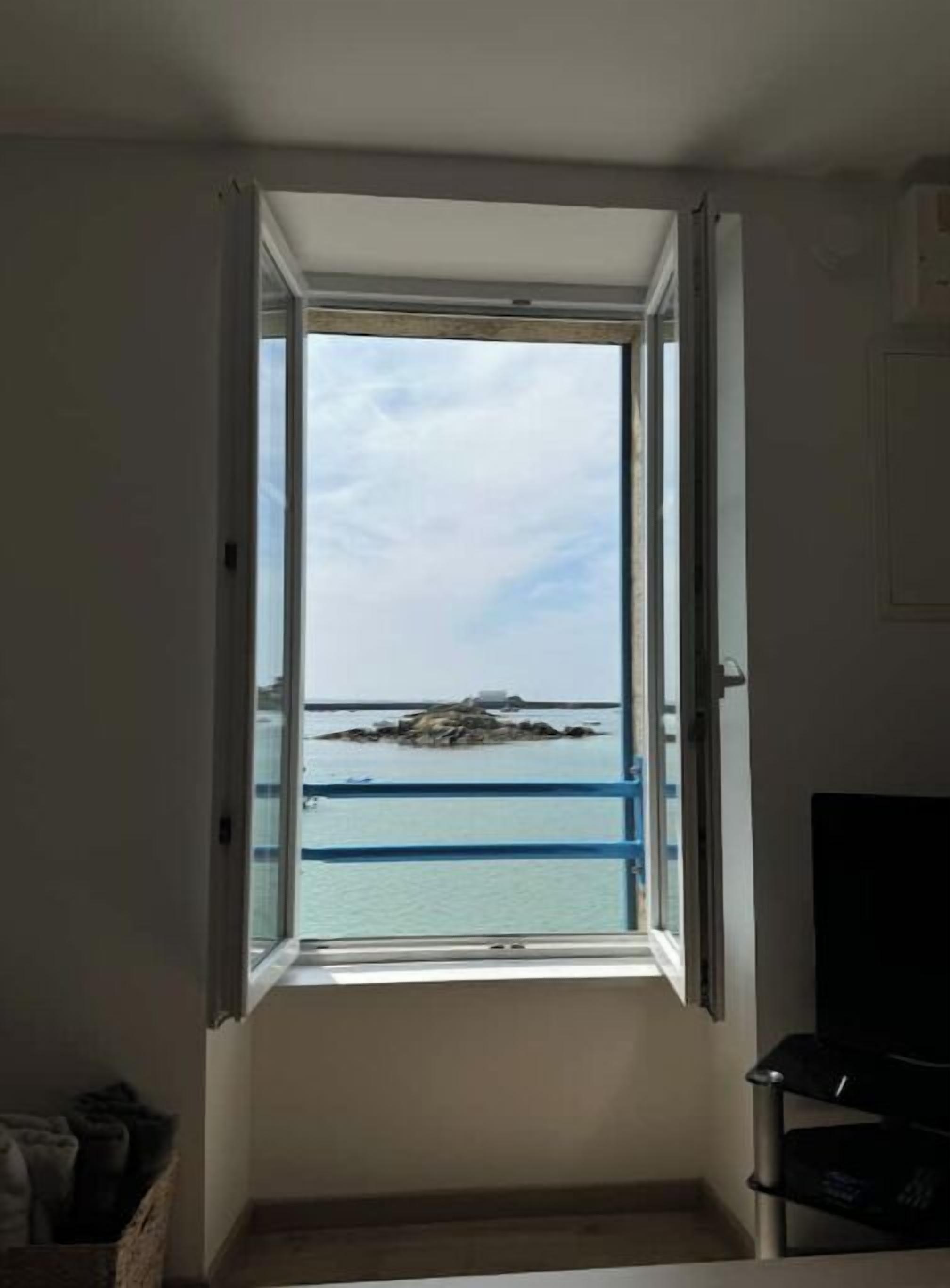 A room with a window overlooking a body of water and a rocky outcrop.