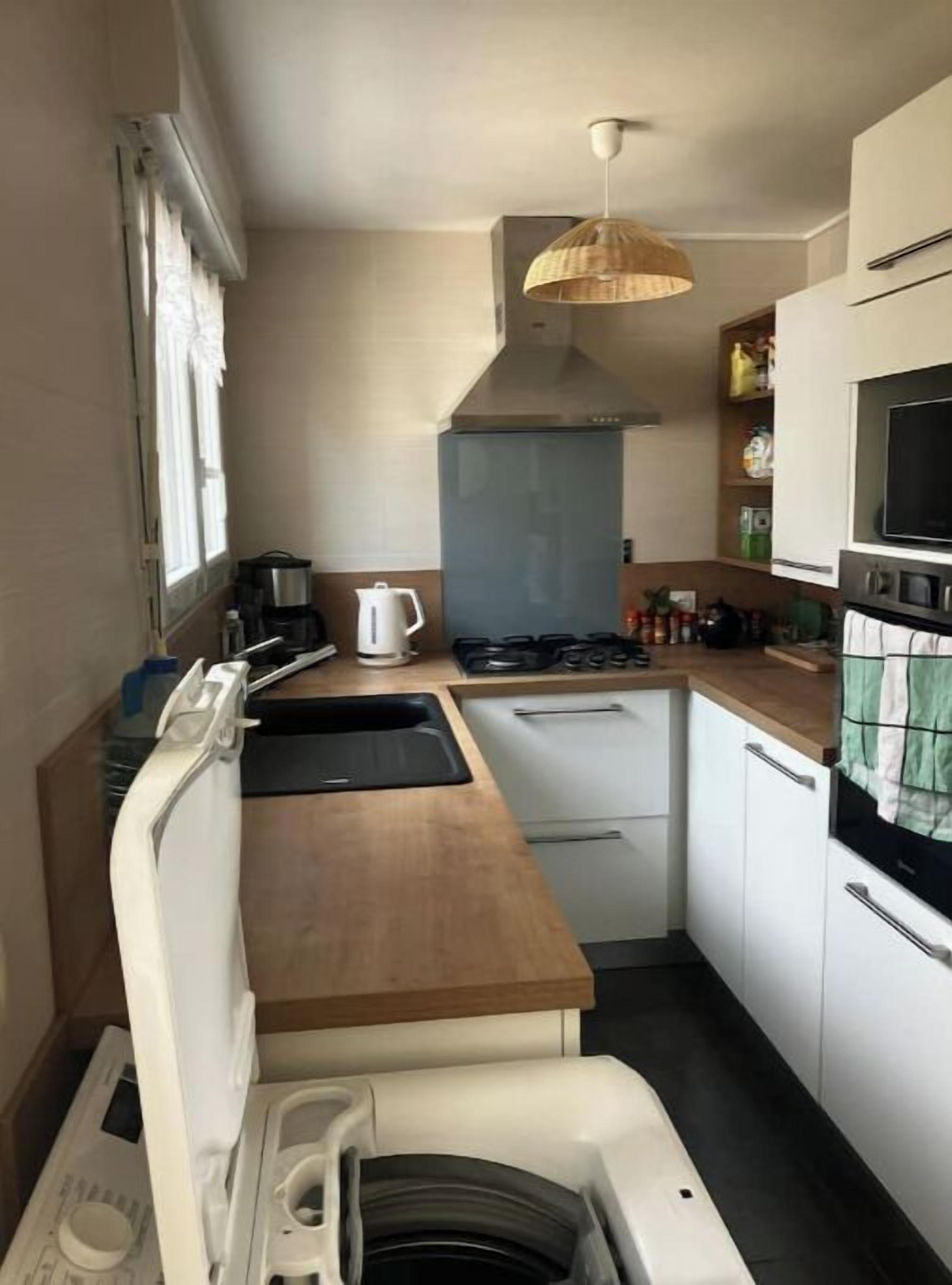 A compact kitchen with a wooden countertop, white cabinets, a built-in oven, and a hanging light fixture.