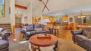 A spacious living room with leather sofas, a round coffee table, and a kitchen in the background.