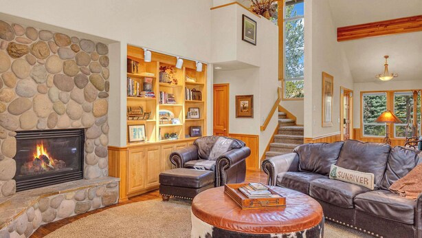A spacious living room with a stone fireplace, leather sofas, a wooden ceiling, and a bookshelf filled with books.