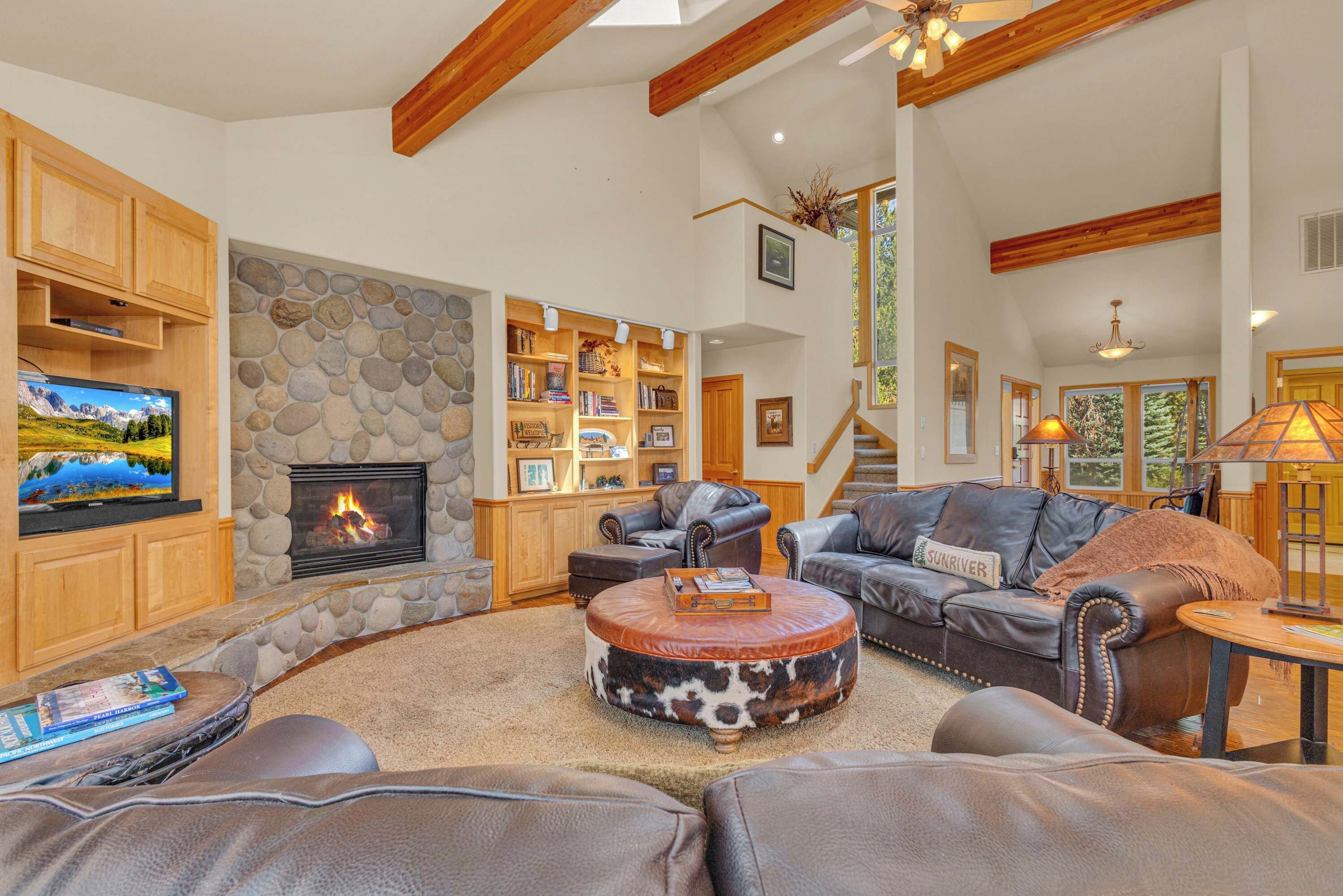 A spacious living room with a stone fireplace, leather furniture, and a bookshelf.