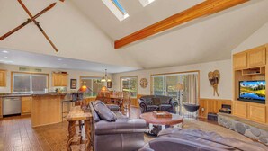 A spacious living area with a wooden ceiling, a large TV, and a stone fireplace.