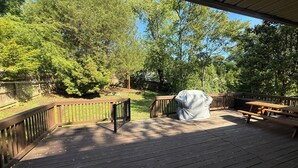Eine überdachte Terrasse im Freien mit einem Grill, Picknicktischen und einem Holzaumschlag.