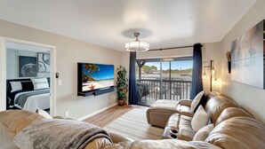 Ett modernt vardagsrum med en stor soffa, en platt-TV och en balkong med utsikt över havet.