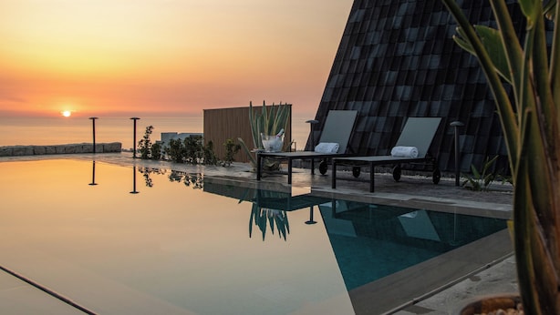 A modern pool area with a sunset view, lounge chairs, and a unique building structure. - Panorama Lodges (Chekka)