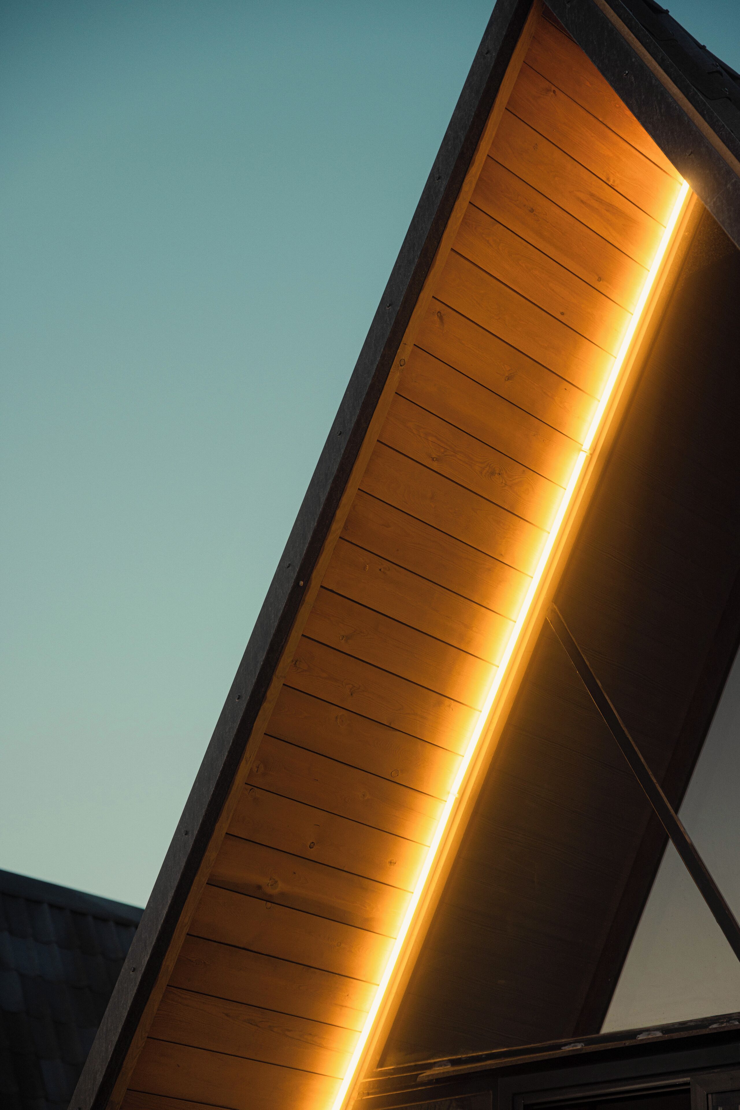 Un edificio moderno con fachada de listones de madera y luz interior visible.