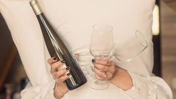 A person holding a wine bottle and two wine glasses, with a pillow in front of them.