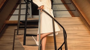 A person standing on a wooden staircase with metal railings, in a room with wooden beams and a sloped ceiling. - Panorama Lodges (Chekka)