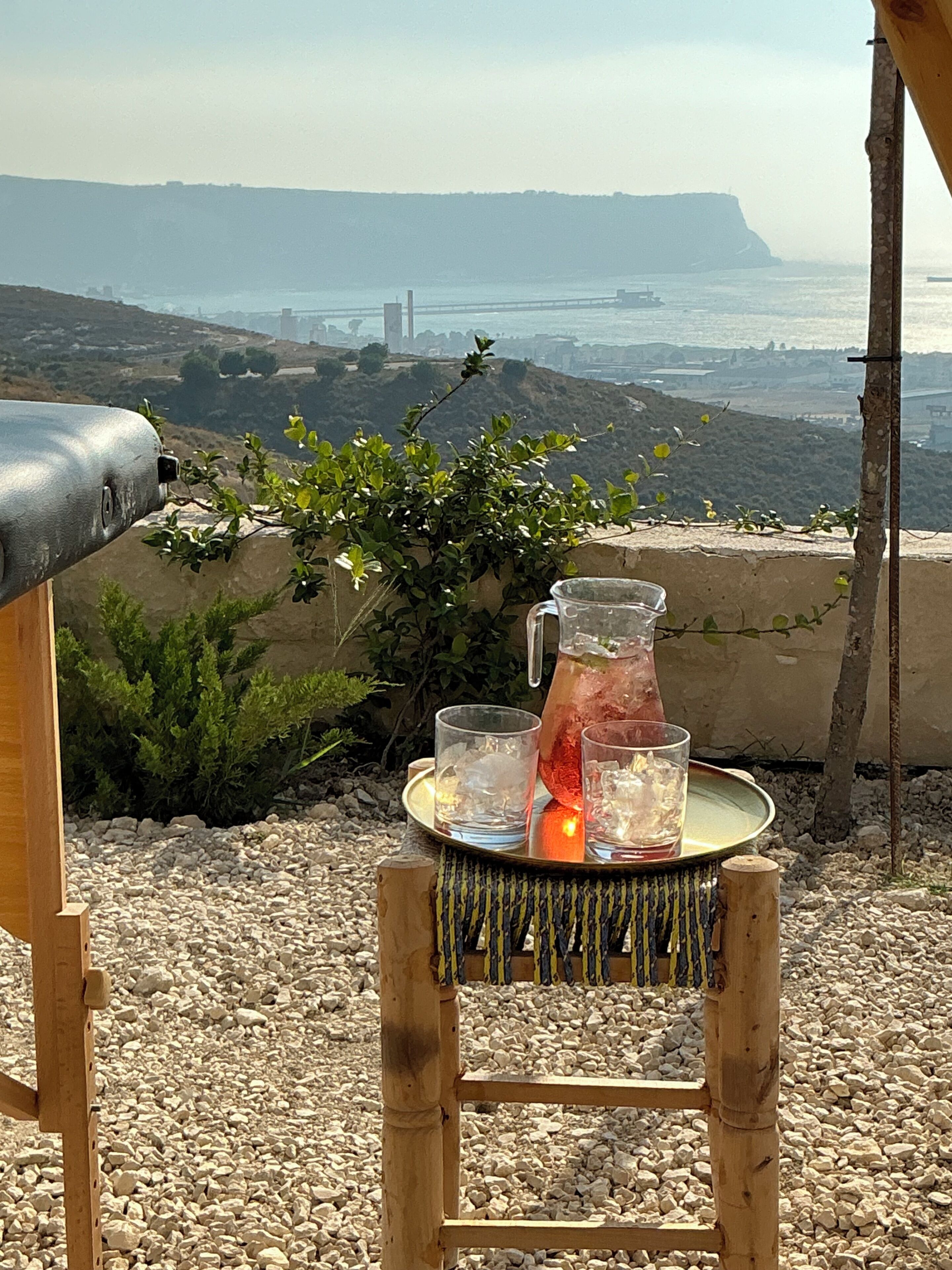 Eine Terrasse mit Grill, einem Holzstuhl und einem Tisch mit einer Karaffe und Gläsern.