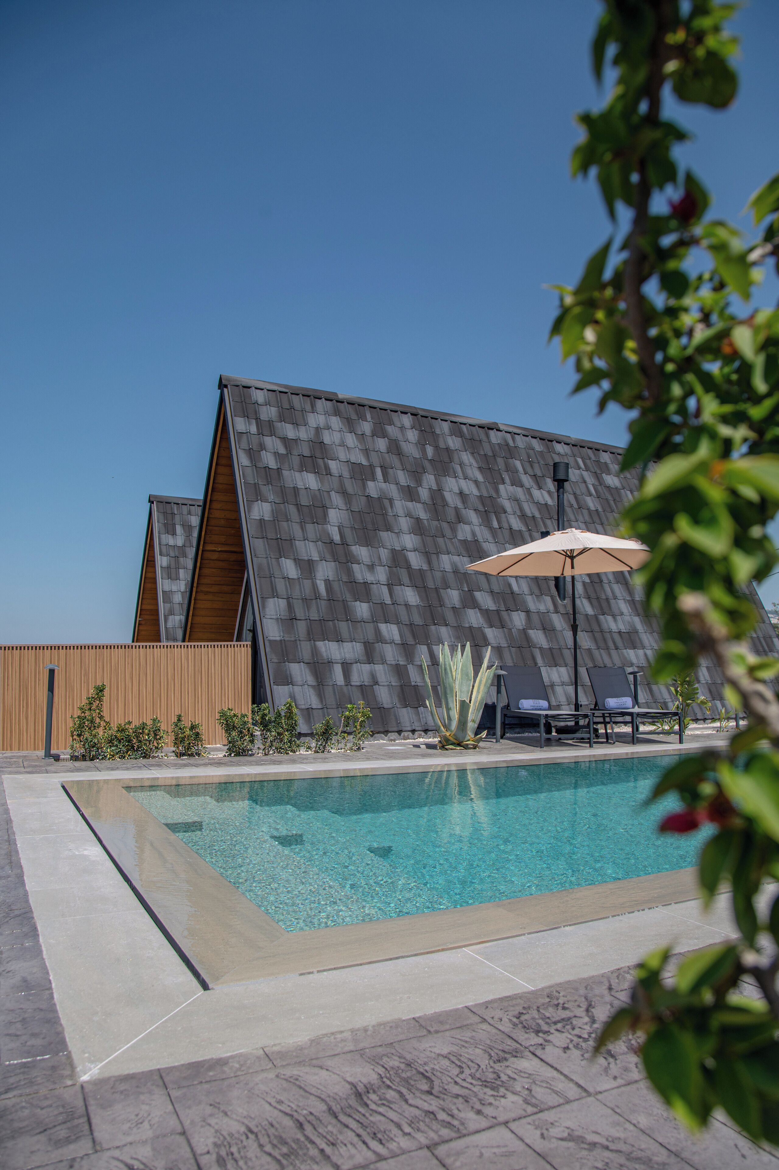 A modern pool area with a clear pool, lounge chairs, and a wooden fence.