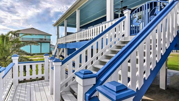 Een houten terras met witte leuningen en blauwe accenten, dat uitkomt op een overdekte veranda.