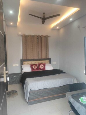 A bedroom with a bed, a ceiling fan, a nightstand, and a small table with a bottle on it. - H&R Paradise Villa (Devanahalli)