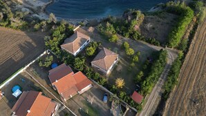 Vue aérienne d’une propriété située sur la côte, avec deux bâtiments principaux, une plage et la végétation environnante.