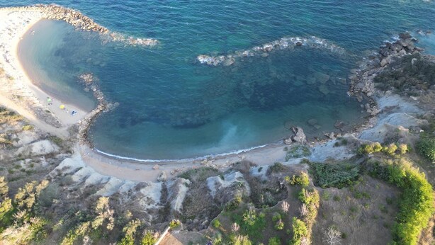 Une vue aérienne d’une zone côtière, avec une mer bleue et limpide, une plage de sable et un terrain rocheux.