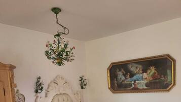 Une chambre à coucher avec un lit à baldaquin blanc, une couvre-lit à carreaux verts, un coussin à motifs floraux, un tableau accroché au mur et une table de chevet en bois.