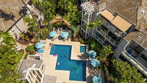 An aerial view of a hotel with a central swimming pool surrounded by lounge chairs and umbrellas, with multiple floors and balconies.