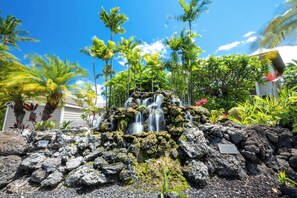 Una cascada que se precipita sobre rocas, rodeada de exuberante vegetación y palmeras.