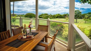 A wooden table with chairs, a bottle of champagne, and a fruit platter.