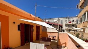 Una terraza en la azotea con una mesa, sillas, un sofá y un paraguas blanco.