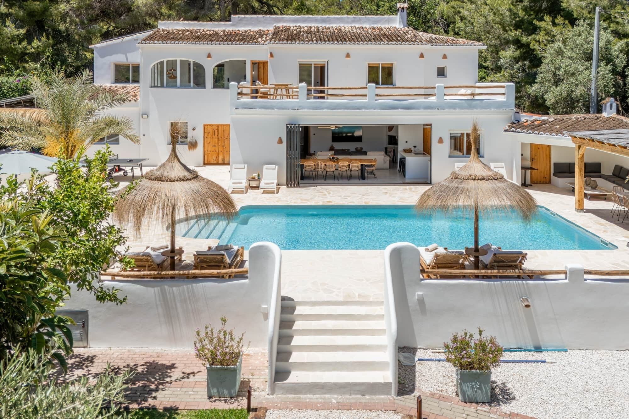 A white villa with a pool, outdoor seating, and a staircase leading to the entrance.
