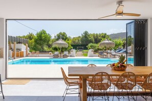 A modern outdoor pool area with a dining table and chairs, a ceiling fan, and a view of the pool and greenery. - Casa Lou Lou - Javea (Xàbia)