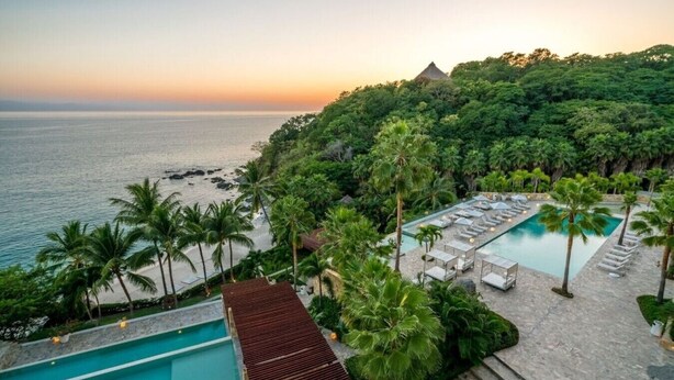 Ein Resort mit Pool, Liegestühlen und Blick auf den Ozean bei Sonnenuntergang.