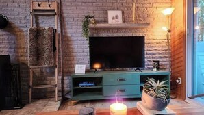Una sala de estar acogedora con pared de ladrillo, un televisor de pantalla plana, mueble de entretenimiento verde, chimenea y una vela sobre una mesa de madera.
