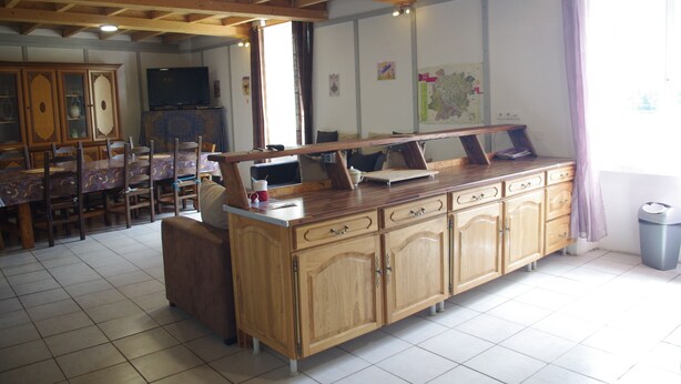 A kitchen with wooden cabinets, a dining table, and a TV. - Gîte Lavardac Estussan (Lavardac)