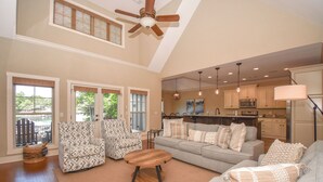A spacious living room with a high ceiling, a large sofa, patterned armchairs, and a wooden coffee table.