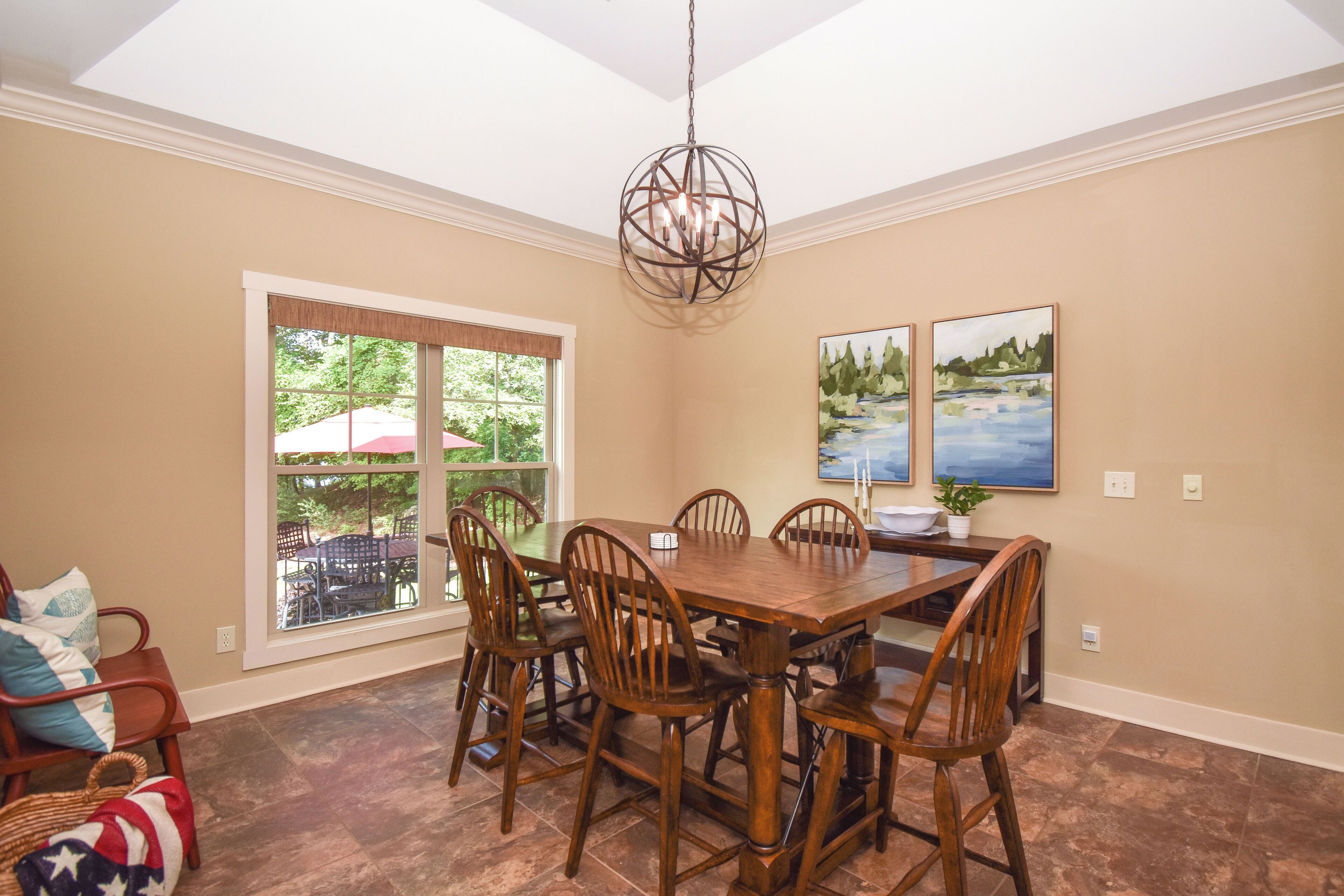 A dining room with a wooden table and chairs, a chandelier, and two paintings on the wall.