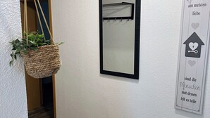 A hallway with a wooden floor, a hanging plant, a framed mirror, and a wall sign with text. - Famielienapartment "An der Forellenschänke " (Sebnitz)