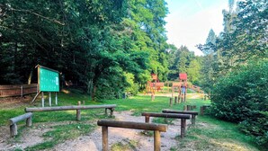 A park with wooden benches, a playground, and a signboard. - Famielienapartment "An der Forellenschänke " (Sebnitz)