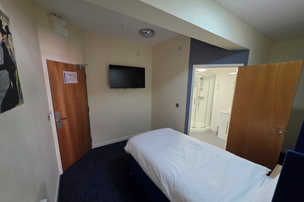 A hotel room with a bed, a television mounted on the wall, and a shower area visible through an open door.