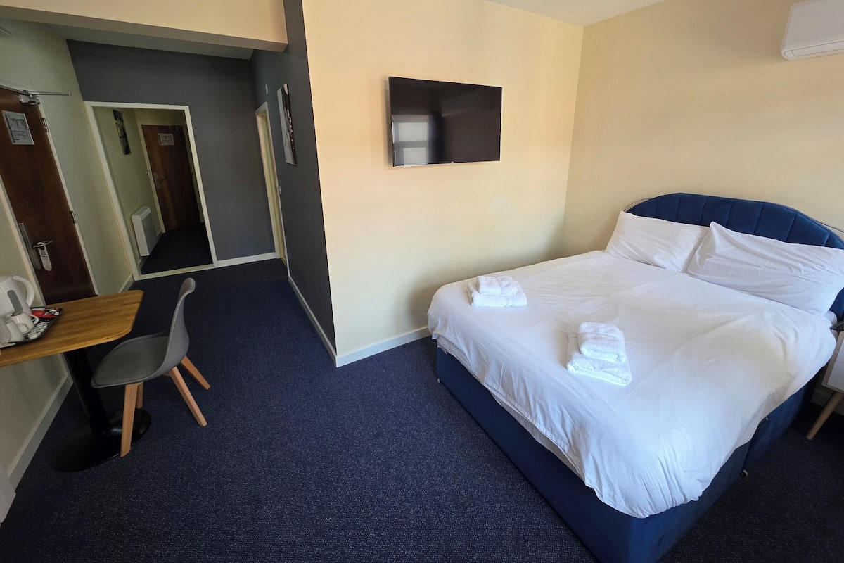 A hotel room with a bed, a desk, a chair, and a flat-screen TV.