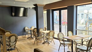 A restaurant interior with wooden flooring, wicker chairs, and tables. There is a large window with a view of the city. - The Carmichael - Hull City Centre (Hull)