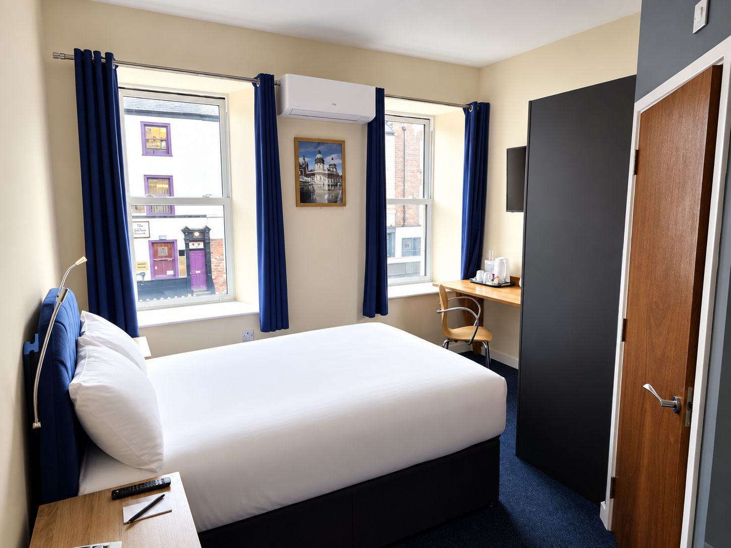 A hotel room with a bed, a desk, a chair, a TV, and a window with curtains.