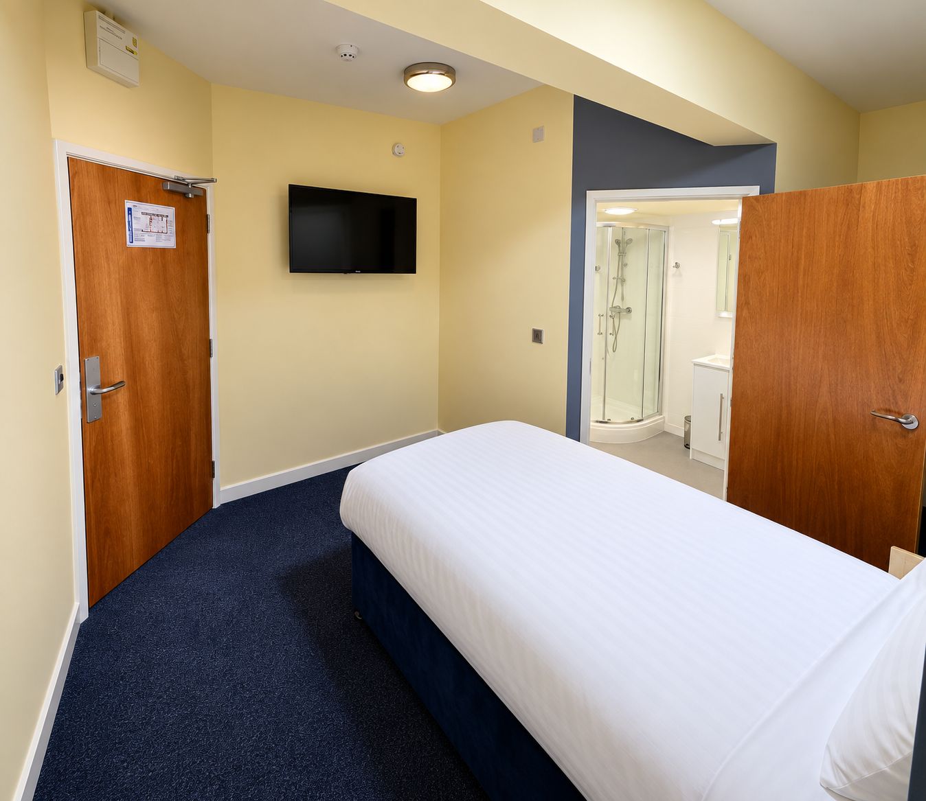 Une chambre d’hôtel avec un lit, un téléviseur fixé au mur et un espace douche visible à travers la porte.